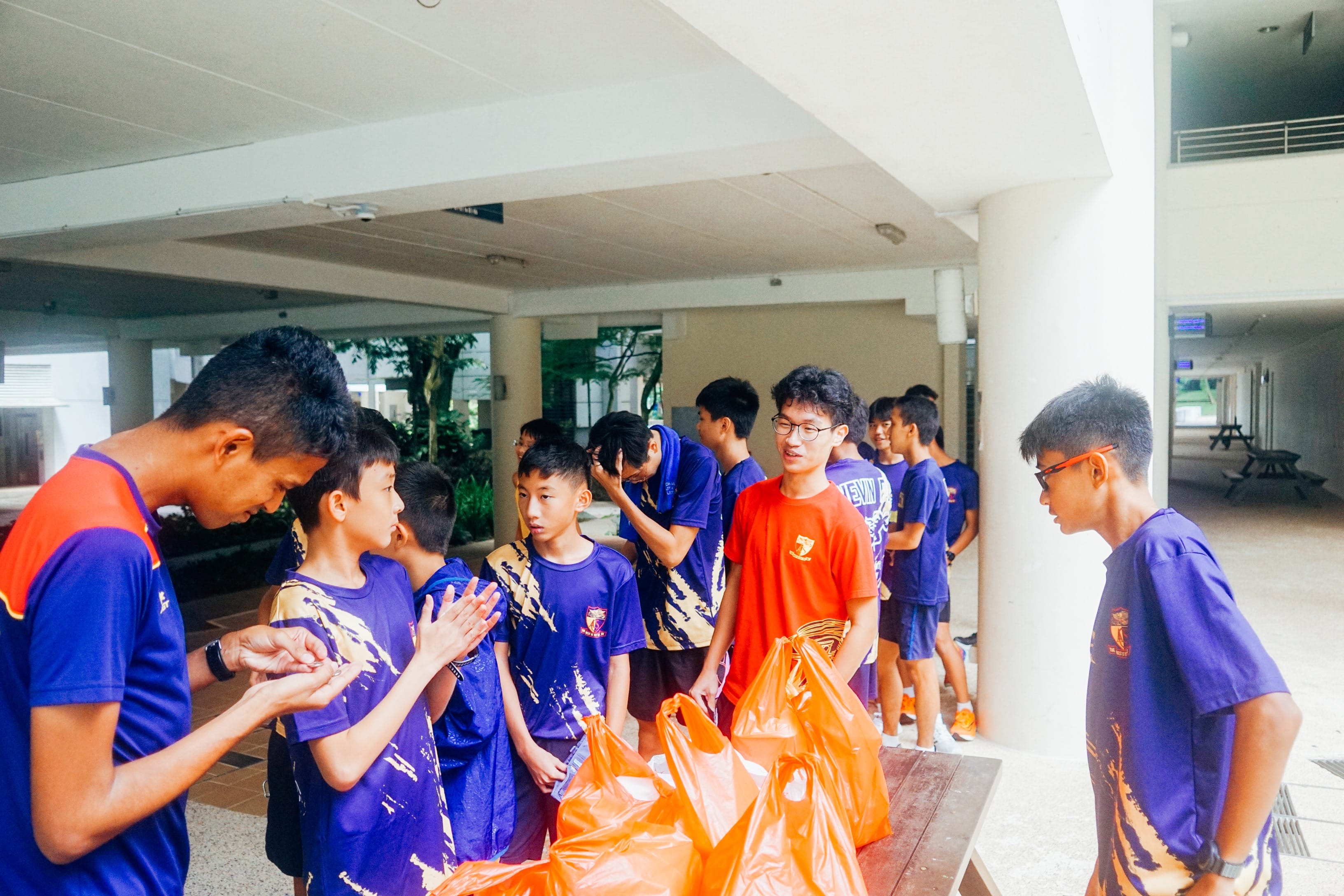 A group of students standing around a table with orange plastic bags on it